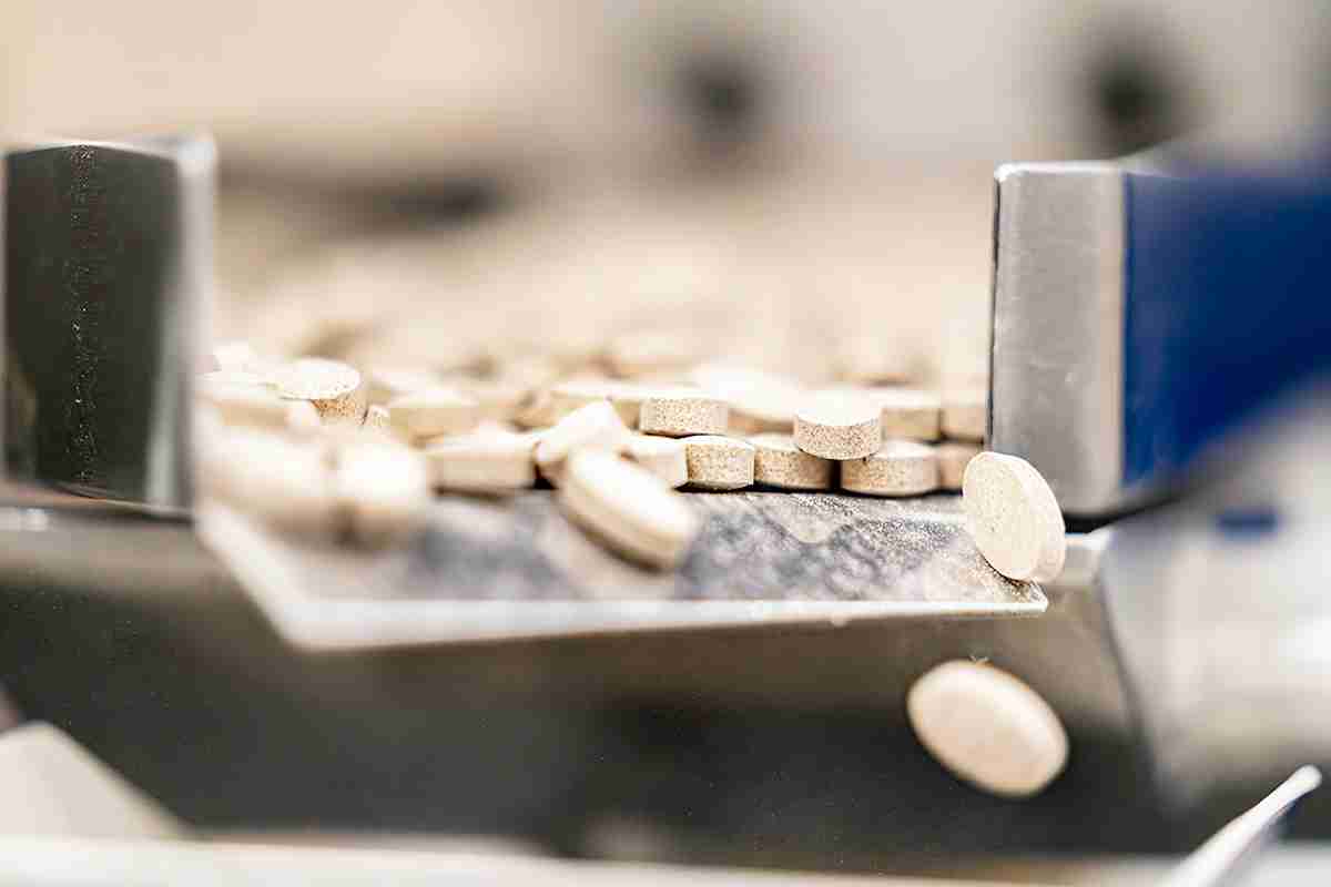 freshly-pressed health supplement tablets spill from the machine exit